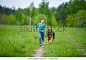 a little boy runs through the green meadow with his big German Shepherd dog. The wind blows his hair