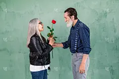 快乐的高级全家福。英俊的胡子老人给美丽的鲜红玫瑰，他的迷人微笑的妻子与长长的灰色直发，站在绿色的墙背