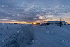 冰岛塞尔福斯的一个住宅区，雪地密布，道路上覆盖着大雪，地平线上升起了太阳，天空阴云密布