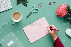 母亲节或生日贺卡设计。手拿笔，在家办公。文字空间，拷贝空间在纸卡上，粉红色的牡丹在绿色的薄荷桌上。咖