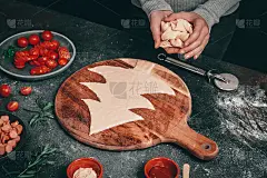 一个白人女孩从切菜板上的披萨面团上分离出一棵圣诞树，手里拿着剩菜