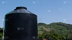 背景是小山的乡村住宅屋顶上的黑色水箱_5200920508