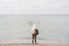冬天，在波罗的海附近的沙滩上，一名年轻的白人男子背着黑色背包。主题的单独旅行。思念和梦想远眺地平线