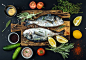 Fresh uncooked dorado or sea bream fish with lemon, herbs, oil, vegetables and spices on rustic...