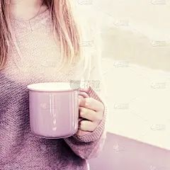 漂亮的金发女人拿着大杯茶站在窗前。早上好，享受阳光吧。家庭生活和幸福理念。健美的形象。