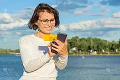 成年女子看了看名片，打了个电话。城市公园背景，河流，天空与云彩