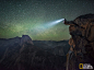 在群星簇拥的夜空之下，一位男士站在冰川点（Glacier Point）的一处名为跳板（Diving Board）的岩层上拍摄下约塞米蒂国家公园（Yosemite National Park）的地貌全景。