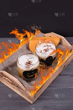 两个玻璃杯子，上面画着万圣节主题的南瓜拿铁，木制托盘上有火焰。饮料的万圣节