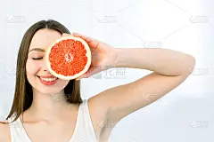 年轻美丽的女人的肖像与健康完美的皮肤拿一块葡萄柚，闭上一只眼睛。天然化妆品、护肤、养生、面部护理、美