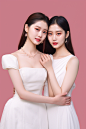 doqae_two_women_in_white_dresses_hugging_in_front_of_a_pink_bac_fd36b08f-7f71-45ea-b9ca-76d6c00a91ad