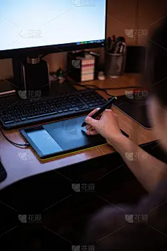 一位女性拿着笔在写字板上工作，在显示器昏暗的灯光下工作