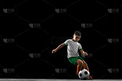 男孩的全身肖像，孩子，足球运动员在统一训练孤立在黑色背景。运球