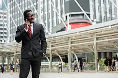 年轻快乐的非洲商人戴着眼镜在曼谷的现代建筑前打电话时面带微笑