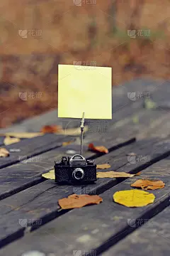 空白纸贴纸与秋天的树叶在老木头的背景。户外书桌古董相机和黄色便条纸
