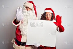 一对老年夫妇穿着圣诞老人服装，高举旗帜，在孤立的白色背景下，张开手做着严肃和自信的表情，防御手势