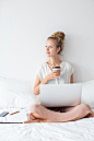 Dreamy Girl Working on Laptop and Drinking on Bed Free Photo