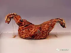 “延年益寿大宜子孙”锦鸡鸣枕

时代:

东汉（公元25~220年）

尺寸:

长50厘米、宽13.5厘米、高9厘米

1959年民丰尼雅遗址1号墓出土

基本完好，局部有血迹。枕由一块“延年益寿大宜子孙”文句锦缝缀，中部是鸡身，两端各有一鸡首。鸡首相背，缝制出了尖嘴、圆眼及冠、细颈等。眼睛由三层圆绢片叠放而成：底为白绢、中上皆为红绢。冠作锯齿状，由天青和白绢组成。枕芯是植物茎杆。