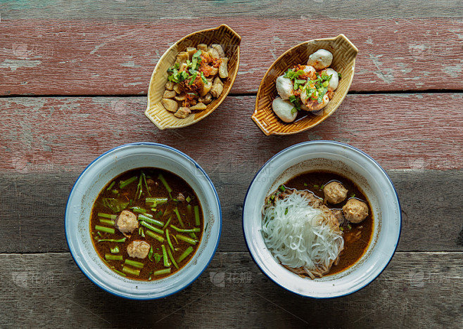 泰式船面“Kuay Tiew Rua”在瓷砖碗里，猪肉皮和猪肉球放在质朴的木桌上。