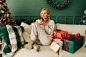 一个漂亮的金发女人坐在圣诞节客厅的沙发上喝咖啡。图片-商业图片-正版原创图片下载购买-VEER图片库