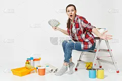 一个女人手里拿着一捆美元，现金，坐在梯子上，手里拿着装修公寓用的工具，孤立在白色背景上。壁纸配件用于