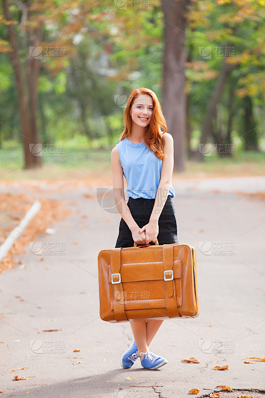 快乐的红发女孩提着手提箱在秋天的公园里。