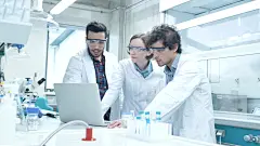 化学教室实验室中穿着大衣的多民族学生使用笔记本电脑的群体