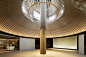 This may contain: a round room with a wooden ceiling and circular lighting fixture in the center, surrounded by white tables