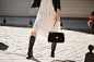 Legs of young pretty woman in boots walking in street in fashionable outfit, holding purse, wearing black leather jacket and white lace dress, spring autumn style