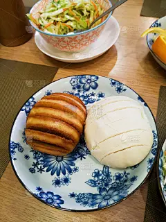 在中餐馆里，青花印花盘子里的中国食物，卷心菜和胡萝卜沙拉，馒头，菠萝和桔子鸡和米饭