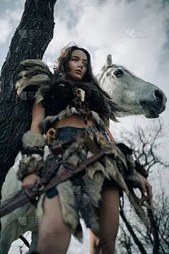一名女子站在森林里，在她的马旁边有一把剑。