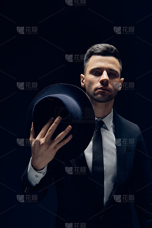 年轻英俊的男子在黑色西装戴着他的帽子在黑...