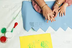 特殊教育的老师和学生穿着长袍，在桌子上用手画着生日花环和涂着丙烯颜料的黄色纸板。塑料工艺疗法。