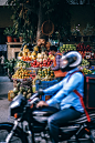Motorcyclist rides past a street vendor stand with fresh fruits and vegetables