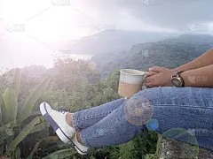 在山景背景上，手拿一杯茶或咖啡，独自坐着的人放松双腿。