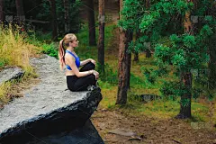 一个金发女人在森林里的一块岩石上做着轻松的冥想。瑜伽的本质概念。
