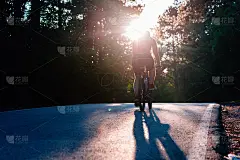 一个男性骑自行车的人骑他的自行车在日落的道路上通过深森林。极限骑手没有安全装备。