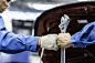 汽车修理工拿着扳手撞拳头与团队同事在汽车修理厂。团队合作理念，为汽车维修服务行业服务。汽车制造业务