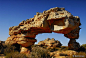 This may contain: an arch shaped rock formation in the middle of a desert area with grass and bushes