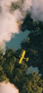 This may contain: an aerial view of a yellow plane flying over trees and water in the sky with clouds