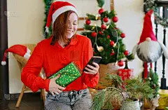 微笑的女人手里拿着手机靠近圣诞树。新年的心情。节日庆祝活动
