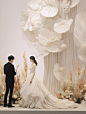 a wedding ceremony taking place with one another in a white stage, in the style of sandara tang, organic sculpting, angelic photograph, floral surrealism, atey ghailan, light beige and black, unique and one-of-a-kind pieces