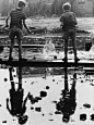 two young boys take great delight in the splashes made by dropping chunks of rubble into a large puddle, 1964
