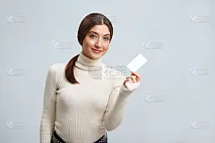 美丽的女孩拿着一张浅灰色背景的名片。年轻女子微笑着。
