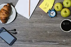 办公配件的背景。记事本，咖啡杯，智能手机，耳机，羊角面包