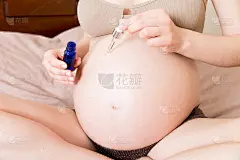 一个怀孕的女孩坐在家里的床上，在她的肚子上涂抹了一种抗妊娠纹霜。怀孕、母性、准备和期望的概念