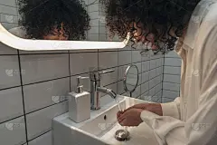 年轻的混血妇女在现代化的盥洗室里洗手和洗脸。卷头发的女人在早上准备好了。