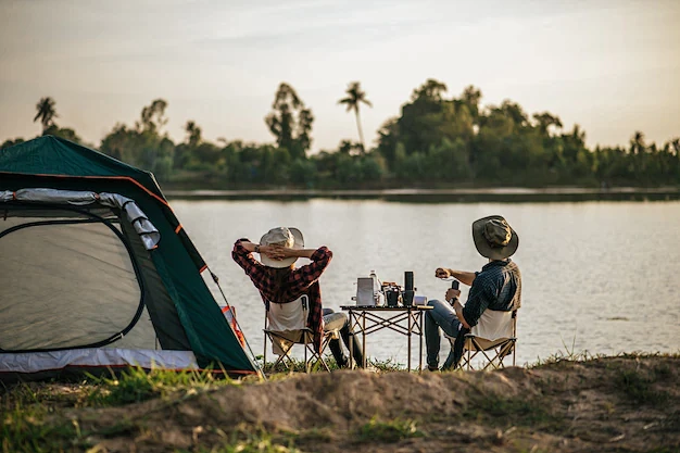 年轻的背包客夫妇坐在靠近湖边的帐篷前放松...