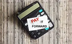计算器和木桌上贴着一张贴纸，上面写着“让爱传出去”(Pay It Forward)的红色文字