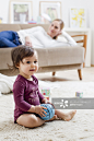 Mother lying on sofa watching baby boy play on floor