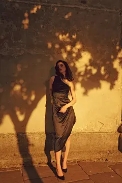 黑发的年轻女子身穿黑色连衣裙，在阳光下闭着眼睛站在街上，树影托着她的连衣裙照片素材_4440525908